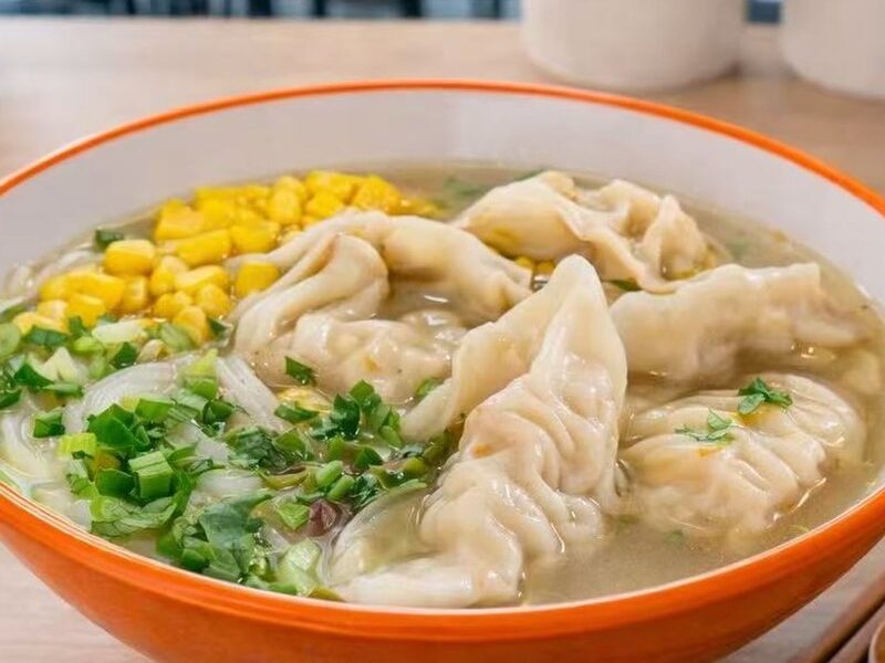 A bowl of wonton soup with corn, scallions and noodles