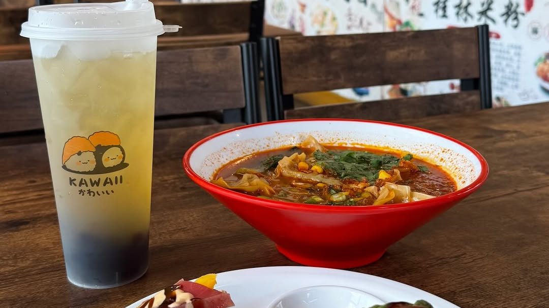 A Kawaii-branded iced tea with boba pearls beside a red bowl of spicy soup on a table at Kawaii Tea Time
